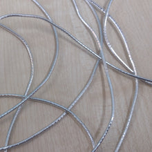 A close-up of several thin silver metal wires or cords loosely coiled on a light wood surface.