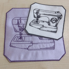 Two embroidered patches featuring line drawings of sewing machines, one in light purple with a dark purple border and one in white with a dark border, placed on a light wood surface.