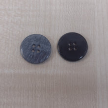 Two round four-hole buttons, one dark gray with a subtle wood grain pattern and the other solid black, placed on a light beige wood-grain surface.