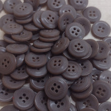 A pile of small, round, four-button brown plastic buttons scattered on a light-colored wooden surface.