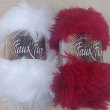 Two skeins of fluffy faux fur yarn, one white and one red, with labels reading 'Faux Fur' on a light wood background.